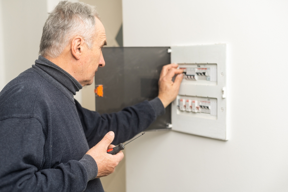 Mature,Man,An,Electrician,Turning,On,Circuit,Breaker,In,Panel.